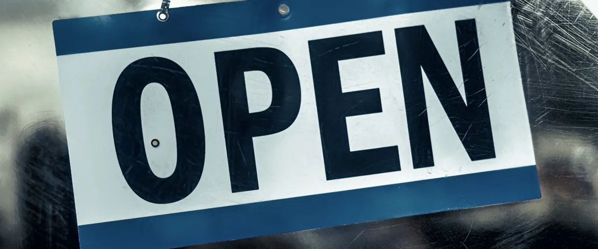 An open sign hanging on the glass door of a new shop